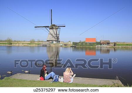 Two Women Sitting on Pier, Windmill in Background View Large Photo Image Stock Photo - Two Women Sitting on Pier, Windmill in Background. Fotosearch