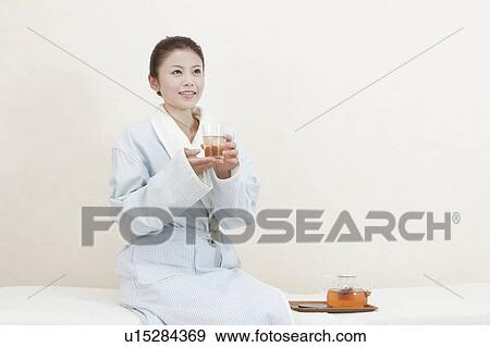 Stock Photo - Woman in bathrobe drinking herb tea. Fotosearch
