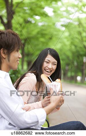 Stock Image - Young couple eating on bench. Fotosearch