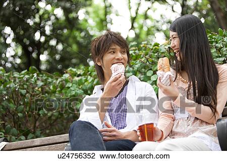 Stock Image - Young couple eating on bench. Fotosearch