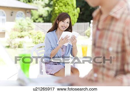 Stock Photo - Young Couple in Garden, Woman Reading Book. Fotosearch