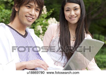 Young couple sitting on a bench using laptop View Large Photo Image Stock Image - Young couple sitting on a bench using laptop. Fotosearch