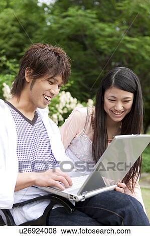 Young couple sitting on a bench using laptop View Large Photo Image Stock Photo - Young couple sitting on a bench using laptop. Fotosearch