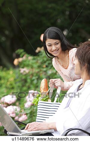Young couple sitting on a bench using laptop View Large Photo Image Stock Photograph - Young couple sitting on a bench using laptop. Fotosearch