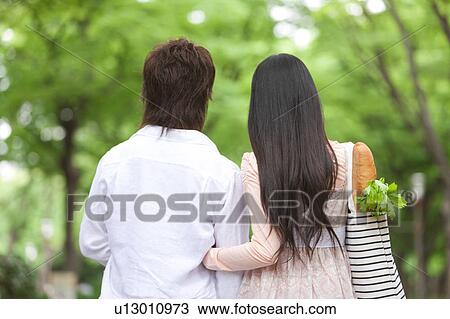 Stock Image - Young couple walking together, rear view. Fotosearch