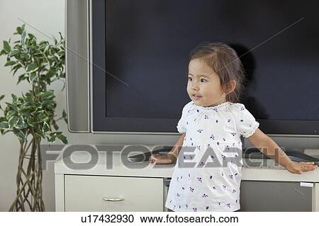 Stock Image - Young Girl Leaning on Television Stand. Fotosearch