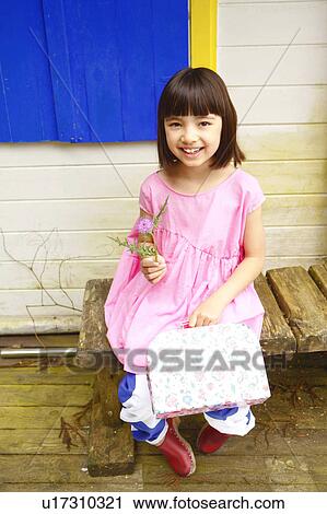 Stock Image - Young Girl Sitting on Bench Outside Playhouse. Fotosearch