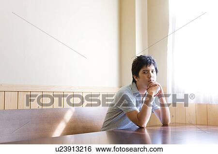 Stock Photograph - Young Man Sitting at Wooden Table. Fotosearch