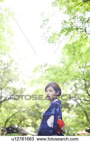 Stock Image - Young Woman in Kimono Standing in Garden. Fotosearch