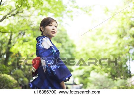 Stock Image - Young Woman in Kimono Standing in Garden. Fotosearch