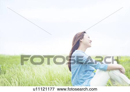 Stock Photo - Young Woman Sitting on Tall Grass. Fotosearch