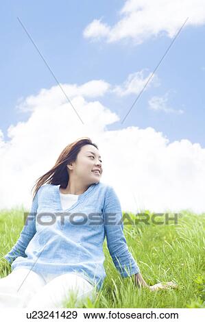 Stock Photo - Young Woman Sitting on Tall Grass. Fotosearch