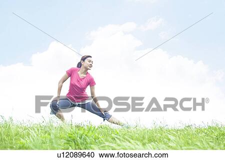 Stock Image - Young Woman Stretching on Grass. Fotosearch