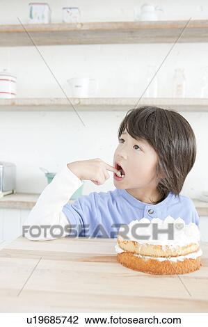 Stock Image - Boy licking an icing on his finger, Hyogo Prefecture, Honshu, Japan. Fotosearch