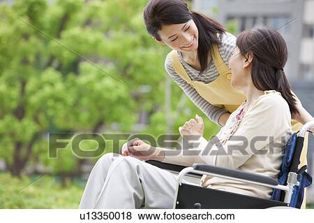 Stock Photo - Caretaker and mature woman on wheelchair talking. Fotosearch