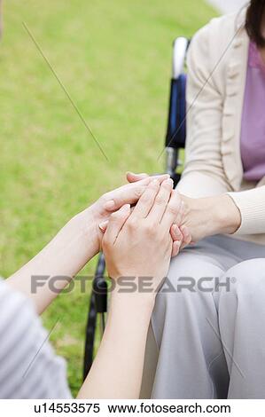 Stock Photography - Caretaker and mature woman on wheelchair holding hands. Fotosearch