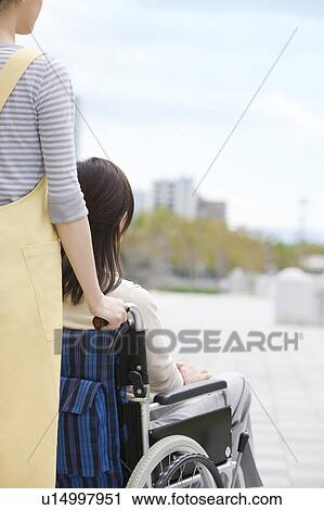 Stock Image - Caretaker pushing mature woman on wheelchair. Fotosearch