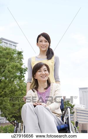 Stock Photograph - Caretaker pushing mature woman on wheelchair. Fotosearch