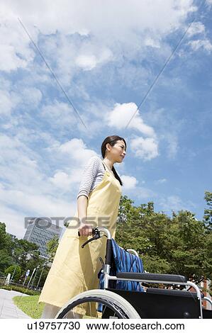 Stock Image - Caretaker pushing wheelchair. Fotosearch