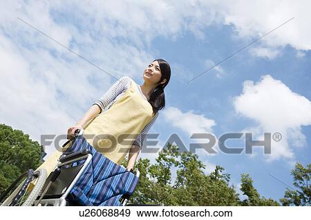 Stock Photo - Caretaker pushing wheelchair. Fotosearch