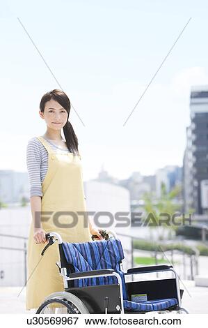 Stock Photo - Caretaker pushing wheelchair. Fotosearch