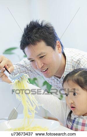 Stock Photo - Father and Daughter Lifting Spaghetti with Tongs. Fotosearch