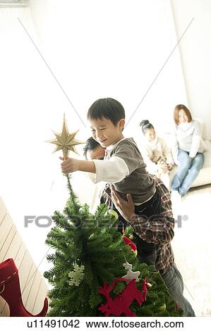 Stock Image - Father Helping Son To Put Star on Christmas Tree. Fotosearch