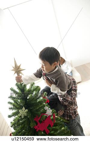 Stock Photo - Father Helping Son To Put Star on Christmas Tree. Fotosearch