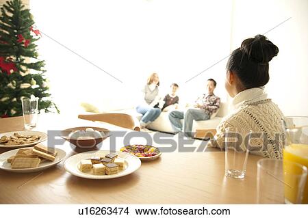 Picture - Girl Sitting at Christmas Table, Family in Background. Fotosearch
