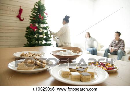 Stock Photograph - Girl Sitting at Christmas Table, Family in Background. Fotosearch