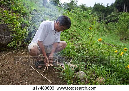 Stock Image - Man Starting Small Fire to Welcome Back Departed Souls of the Bon Festival. Fotosearch