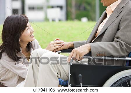 Stock Photography - Mature woman and senior man on wheelchair holding hands. Fotosearch