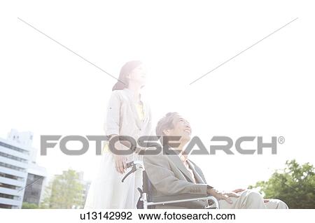 Stock Image - Mature woman pushing senior man on wheelchair. Fotosearch