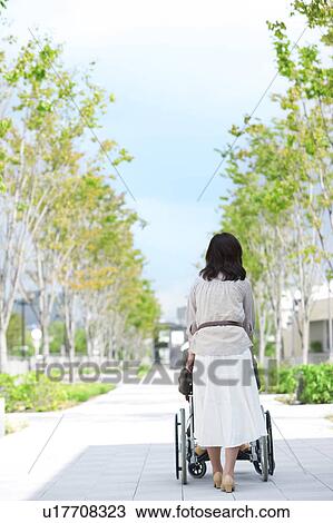 Stock Image - Mature woman pushing senior man on wheelchair, rear view. Fotosearch