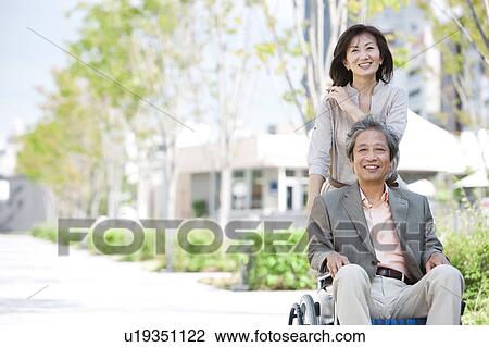 Stock Image - Mature woman pushing senior man on wheelchair. Fotosearch