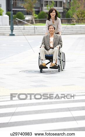 Stock Image - Mature woman pushing senior man on wheelchair. Fotosearch