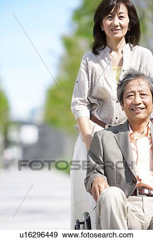 Stock Photo - Mature woman pushing senior man on wheelchair. Fotosearch