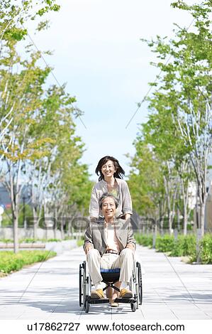 Stock Photo - Mature woman pushing senior man on wheelchair. Fotosearch
