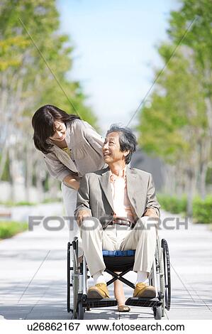 Stock Photo - Mature woman pushing senior man on wheelchair. Fotosearch