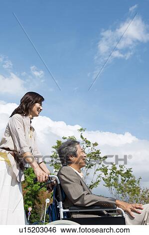 Stock Photograph - Mature woman pushing senior man on wheelchair. Fotosearch