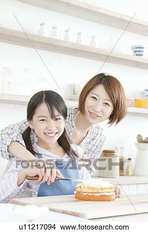 Picture - Mother and daughter in kitchen decorating cake, Hyogo Prefecture, Honshu, Japan. Fotosearch