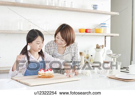Picture - Mother and daughter in kitchen decorating cake, Hyogo Prefecture, Honshu, Japan. Fotosearch