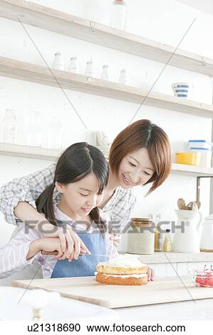 Stock Image - Mother and daughter in kitchen decorating cake, Hyogo Prefecture, Honshu, Japan. Fotosearch