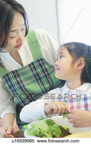 Stock Photography - Mother and Daughter Looking at Each Other and Preparing Salad. Fotosearch