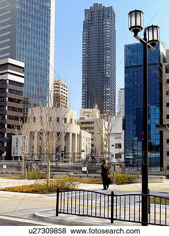 Stock Photo - Person Standing in Town Square Surrounded by Skyscrapers. Fotosearch