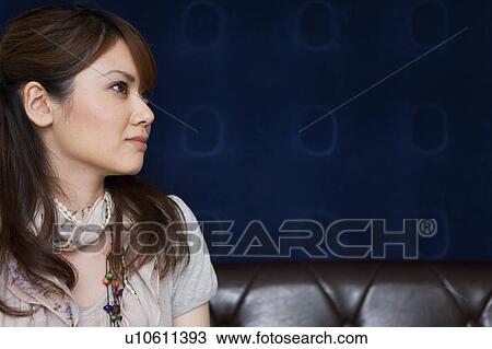 Stock Image - Profile of young woman sitting on sofa. Fotosearch