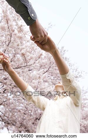 Stock Image - Rear view of couple holding hands, low angle view. Fotosearch