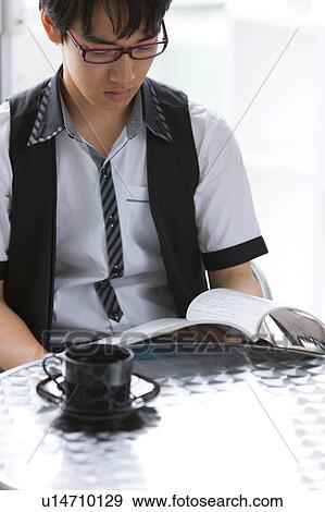 Stock Photo - Young man reading a magazine at a cafe. Fotosearch