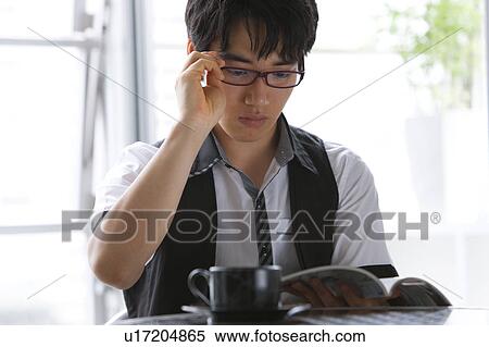 Young man reading a magazine at a cafe View Large Photo Image Stock Photography - Young man reading a magazine at a cafe. Fotosearch