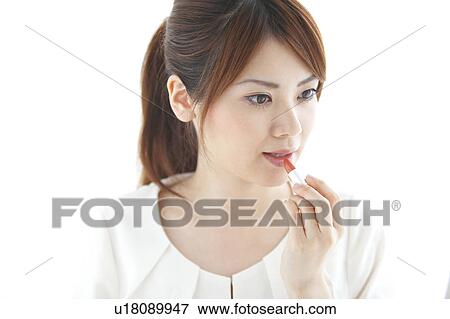 Stock Photo - Young woman applying lipstick. Fotosearch